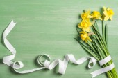 view from above of bouquet of daffodils wrapped by white ribbon on green background