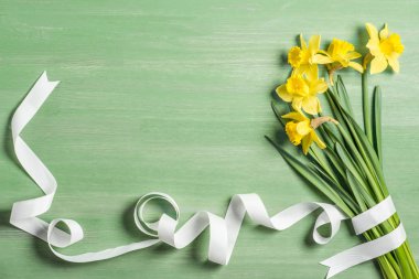 view from above of bouquet of daffodils wrapped by white ribbon on green background clipart