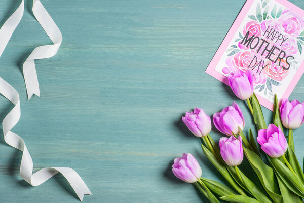 верхний вид на белую ленту, букет тюльпанов и открытка с надписью счастливый день матери на синем фоне
 