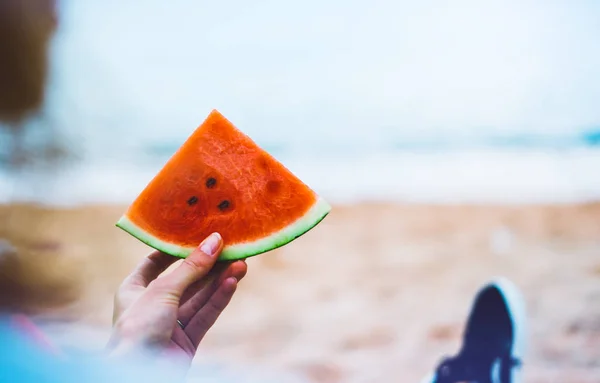 young girl hipster relax on beach coast and holds in her hand a slice of red fresh fruit watermelon on blue sea background, woman on seaside nature eating sweet healthy food, vacation in summer concept