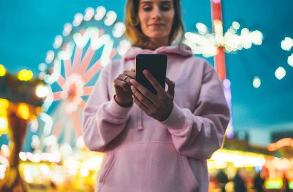 Front view girl pointing finger on screen smartphone on defocus background bokeh light in evening street attraction, woman using in hands mobile phone gadget in night city illumination, online wifi internet concept
