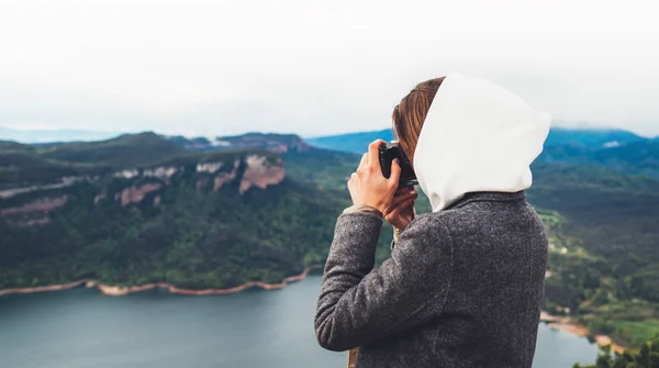 photographer tourist traveler standing on green top on mountain holding in hands digital photo camera, hiker view from back taking photography, girl enjoy nature panoramic landscape in trip, relax holiday hobby concept