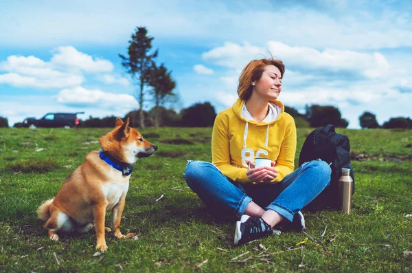 Happy smile girl holding in hands cup drink, red japanese dog shiba inu on green grass in outdoors nature park, beautiful young woman hipster and dogs friends, friendship lifestyle relax recreation meditation concept