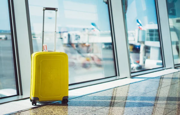 isolate traveler tourist yellow suitcase at floor airport on background large window, bright luggage waiting in departure lounge area hall of airport lobby terminal, vacation trip concept, empty space mockup
