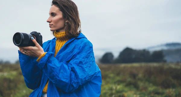 photographer tourist girl in blue raincoat hold in female hands photo camera take photography froggy mountain, traveler shooting autumn nature, click on camera technology, journey landscape vacation concept free space