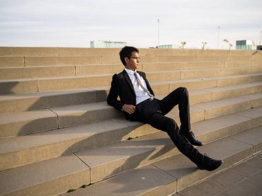 Güney Amerikalı adam açık merdivenlerde oturan bir takım elbise giymiş