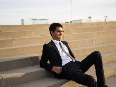 Güney Amerikalı adam açık merdivenlerde oturan bir takım elbise giymiş