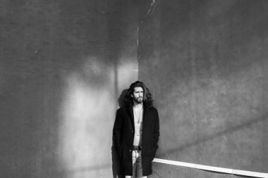 Genç adam gri duvar üzerinde siyah palto poz çıplak gövde ile sakallı