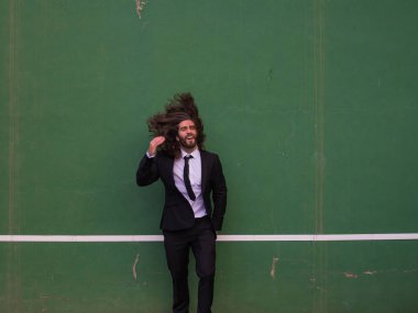 Vahşi yeşil duvar önünde siyah takım elbise atlama adam sakallı