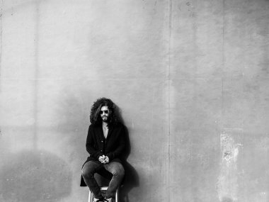 Genç adam gri duvar üzerinde siyah palto poz çıplak gövde ile sakallı