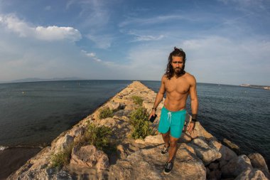 Genç kaslı adam mavi kayalık deniz defne poz