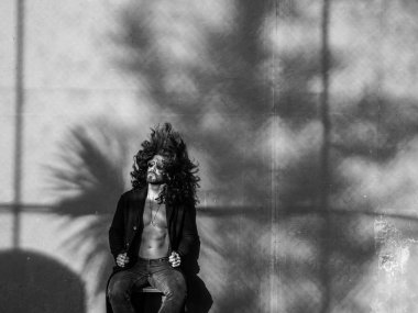 Genç adam gri duvar üzerinde siyah palto poz çıplak gövde ile sakallı