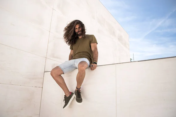 Junger Mann Mit Langen Haaren Sitzt Auf Kalksteinmauer — Stockfoto