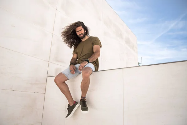 Young man with long hair sitting on limestone wall