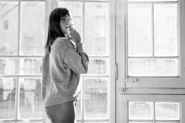 Young woman in sweater smoking cigarette in front of vintage window