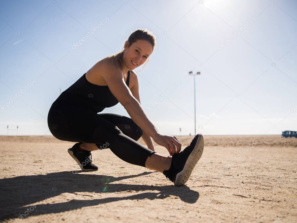 attractive smiling sportswoman stretching legs on beach