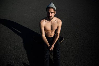 kaykay üzerinde oturan şapka yakışıklı gömleksiz adam