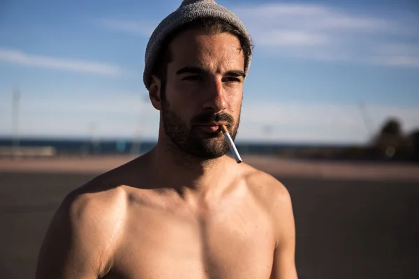 handsome shirtless man in hat smoking cigarette