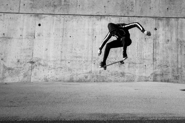 male skateboarder jumping on skateboard at urban place, black and white photo 