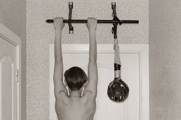 Genç bir adam bir apartman dairesinde yatay bir çubuğa yanaşıyor.