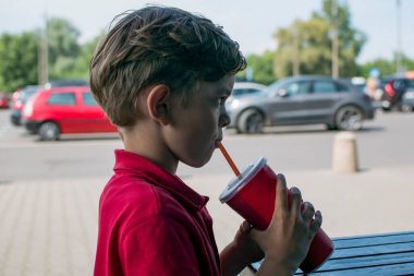 Küçük bir çocuk yazlık bir kafede oturuyor ve serinletici bir içki içiyor.