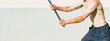 Orta yaşlı bir adam metal bir sopayla egzersiz yapıyor.