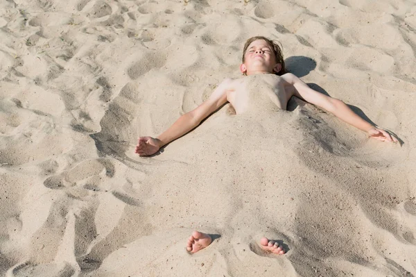 Küçük bir çocuk kumsalda gömülü yatıyor.