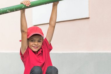 Kırmızı tişörtlü ve şapkalı küçük bir çocuk kameraya poz veriyor.