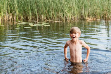 Küçük bir çocuk orman gölünde yüzüyor.