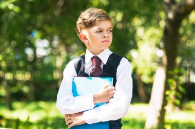 Elinde kitap olan üniformalı küçük bir çocuk okula hazırlanıyor.