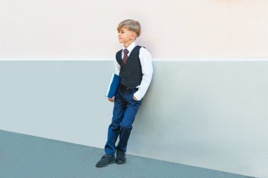 Elinde kitap olan üniformalı küçük bir çocuk okula hazırlanıyor.