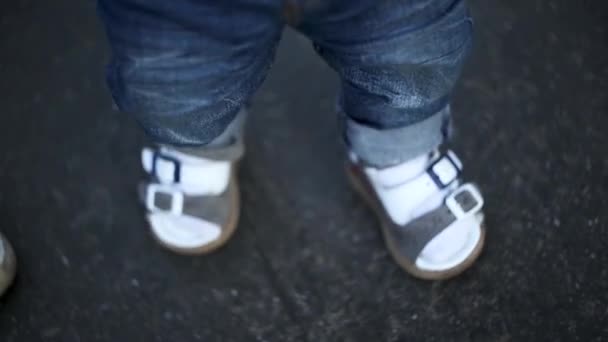 Ноги хлопчика крупним планом навчитися робити перші кроки на асфальтній дорозі — стокове відео