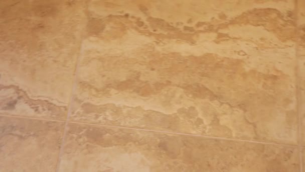 La cámara se mueve suavemente a lo largo de una baldosa de cerámica de color beige en la casa a la luz del día. textura de azulejos del piso de cerca — Vídeos de Stock