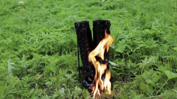 Botas de cuero viejo negro alto punk para mujer queman con fuego de pie sobre la hierba en el parque. concepto viejo zapatos incómodos — Vídeos de Stock