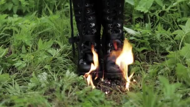 Botas de cuero viejo negro alto punk para mujer queman con fuego de pie sobre la hierba en el parque. concepto viejo zapatos incómodos — Vídeo de stock