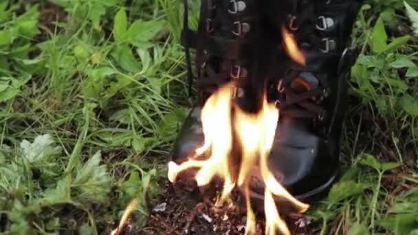 Vieux cuir noir haute punk femmes bottes brûlent avec le feu debout sur l'herbe dans le parc. concept vieilles chaussures inconfortables — Video