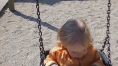Sarı ceketli sevimli küçük kız oyun alanında salıncakta. Yaz aylarında parkta dinlenen neşeli çocuk.