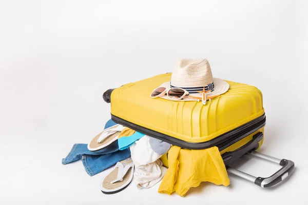 Muts en zonnebril op een gele koffer met kleren van de reiziger op een witte achtergrond. Reis-en avonturen concept — Stockfoto