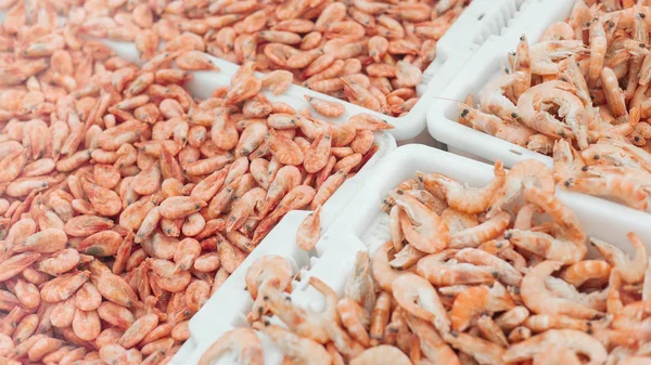 Pink fresh frozen shrimps with ice in a supermarket or fish shop. Uncooked seafood close up background. Fresh frozen prawns, delicacies, sea food concept,