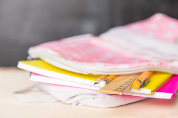 bright open school bag with school supplies lies on a desk against the background of a school blackboard