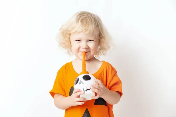 Щасливого Хеллоуїна. кучеряве смішне дівчинка в гарбузовому костюмі п'є коктейль з черепа на білому тлі — стокове фото