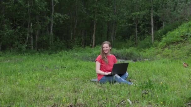 Біла дівчина на відкритому повітрі в парку працює на ноутбуці, собаці нудно з нею — стокове відео