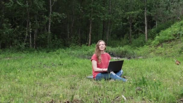 Caucasiano menina está sentado ao ar livre no parque trabalhando em um laptop — Vídeo de Stock