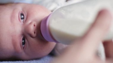 Beslenme şişesinden süt içen küçük şirin bir bebeğin yakın plan portresi.