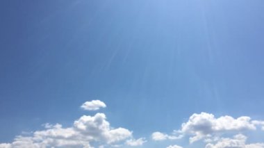 Mavi gökyüzündeki sıcak güneşte beyaz bulutlar kaybolur. Hızlandırılmış hareket bulutları, mavi gökyüzü arkaplanı ve güneş.