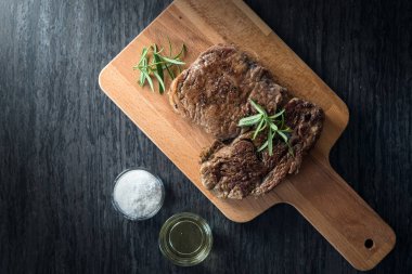 Otlar, tuz ve yağ ile kara tahta üzerinde biftek dilimlenmiş apetisant