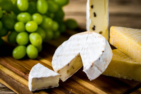 Appetizing cheese with grapes on wooden background