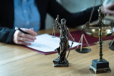 Önplanda hukukun ve adaletin sembolleriyle masada çalışan yargıç