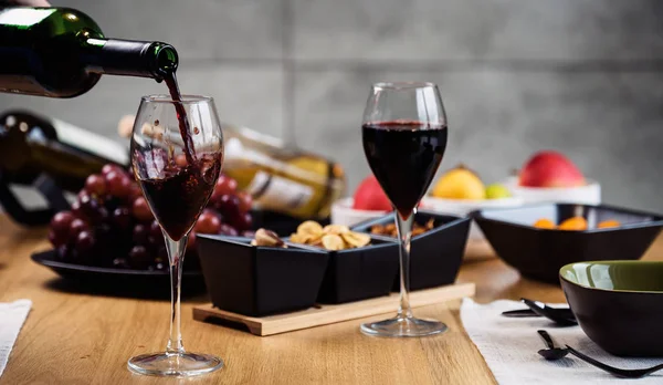 stock image Closeup of pouring red wine with appetizers on background