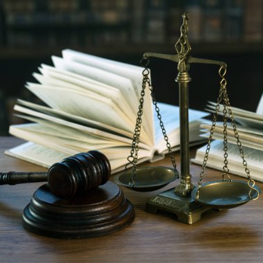 Hukuk ve Adalet sembolleri ahşap masa üzerinde bulanık kitap arkaplanı.